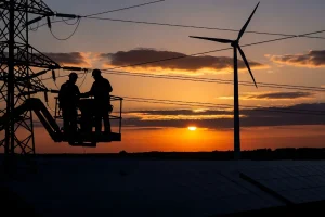Engineers working on power lines at sunset with wind turbine and solar panels in background