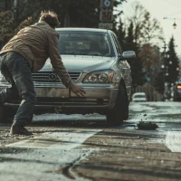 a-person-in-a-beige-jacket-falls-near-a-silver-sedan-on-a-city-street a-person-in-a-beige-jacket-falls-near-a-silver-sedan-on-a-city-street