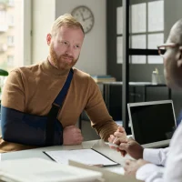 portrait-of-man-with-hand-in-sling-talking-to-insurance-broker-after-workplace-injury-or-accident portrait-of-man-with-hand-in-sling-talking-to-insurance-broker-after-workplace-injury-or-accident