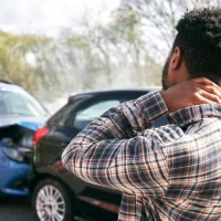 young-male-driver-with-whiplash-injury-standing-by-damaged-car-after-road-traffic-accident